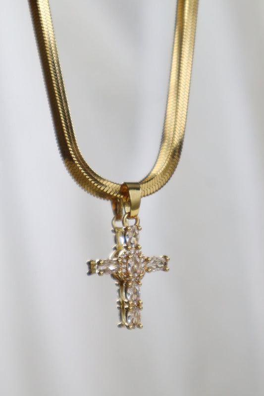 A gold chain necklace with a gold cross pendant embellished with clear rhinestones, displayed against a soft white background.