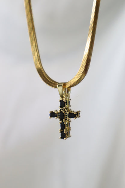 A gold snake chain necklace with a gold cross pendant featuring black rectangular stones, shown against a plain light gray background.